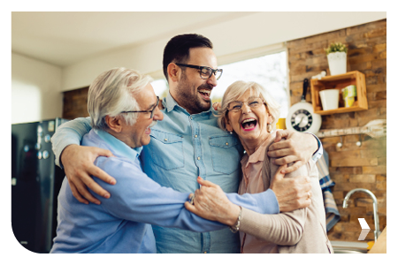 Cheerful mid-adult man and his senior parents laughing while embracing in the kitchen